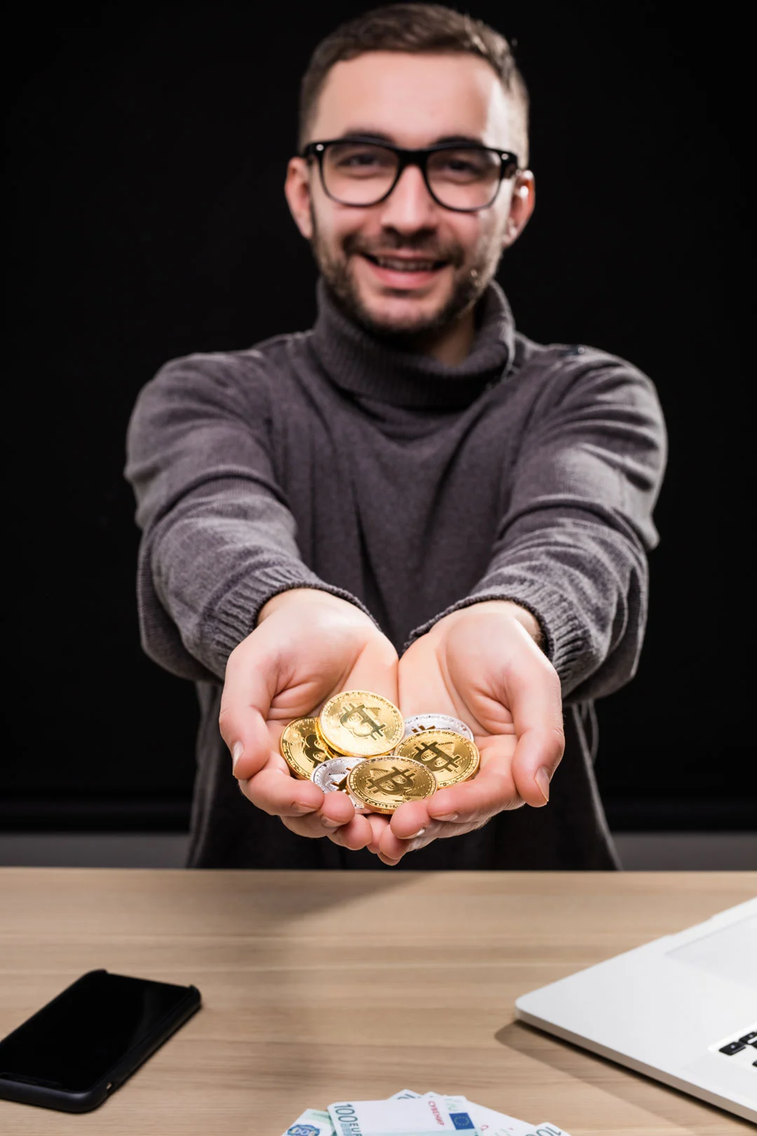 Portrait man glasses showing golden bitcoins his hands desk isolated black